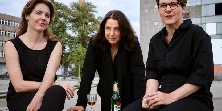 Die Autorinnen Annett Gröschner, Peggy Mädler und Wenke Seemann mit Getränken auf einem Platz vor Plattenbauten