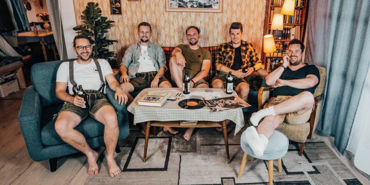 Bandmitglieder von D'Hundskrippln in einem typisch bayerischen Wohnzimmer in Lederhosen  ©Agentur
