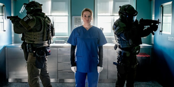 Szene aus Theresa Wolff: Die Gerichtsmedizinerin steht in ihrem Labor, links und rechts zielen SEK-Polizist:innen mit Waffen zur Seite