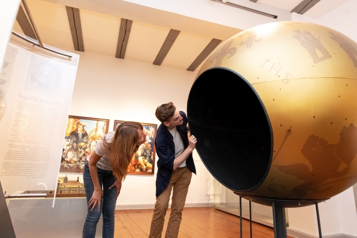 Zwei Besucher:innen betrachten das goldene Modell der Weigelschen Himmelkugel im Stadtmuseum Jena