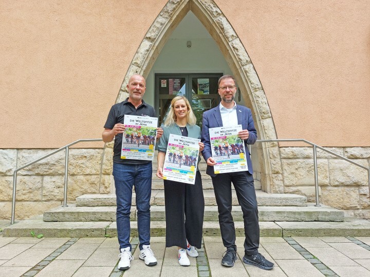 Oberbürgermeister und Sportbeauftragte der Stadt Jena sowie Renndirektor stehen vor dem Rathaus Jena und halten Plakate für die Lotto Ladys Thüringen Tour 2024 hoch 