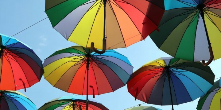 Schwebende Regenschirme mit Regenbogenfarben vor blauem Himmel