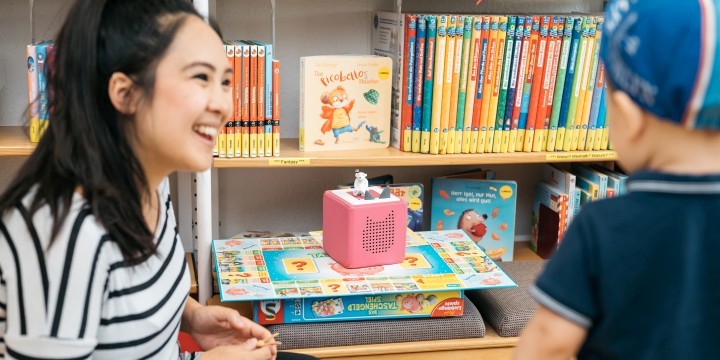 Junge Frau mit kleinem Kind vor einem Regal mit Medien für Kinder in der Stadtteilbibliothek Lobeda